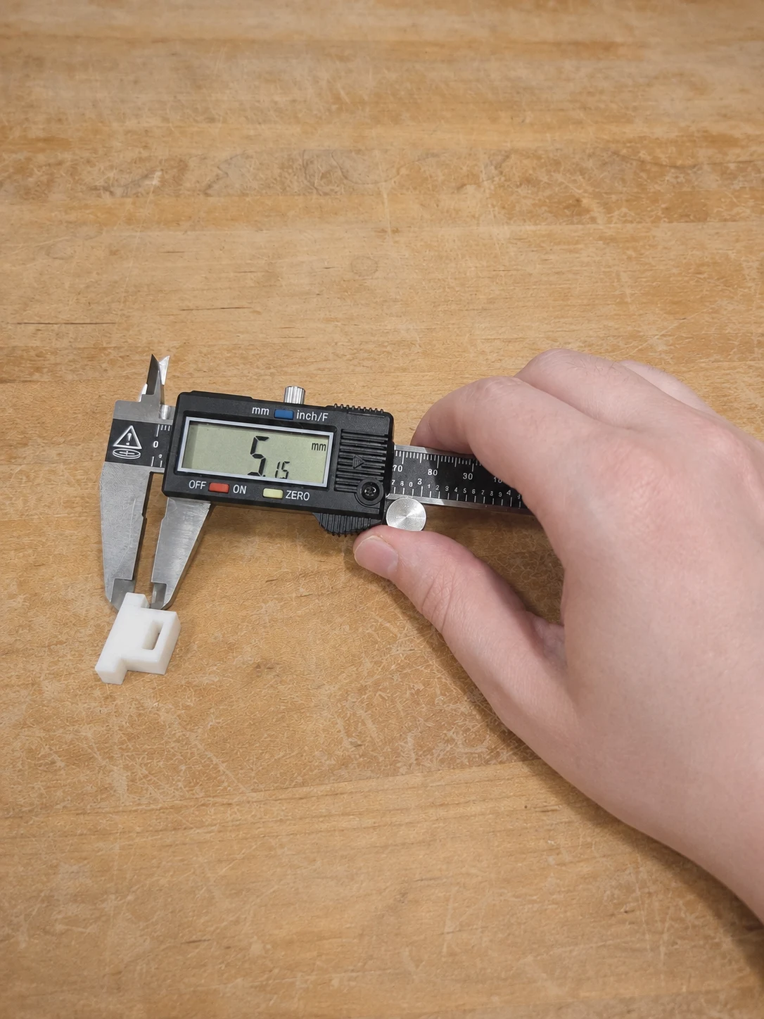 Real shop photograph of a white printed part being measured with digital calipers
